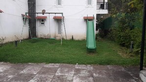 A backyard with a green slide, a swing set, and a small window. - KODAI FOGGY (Kodaikanal)