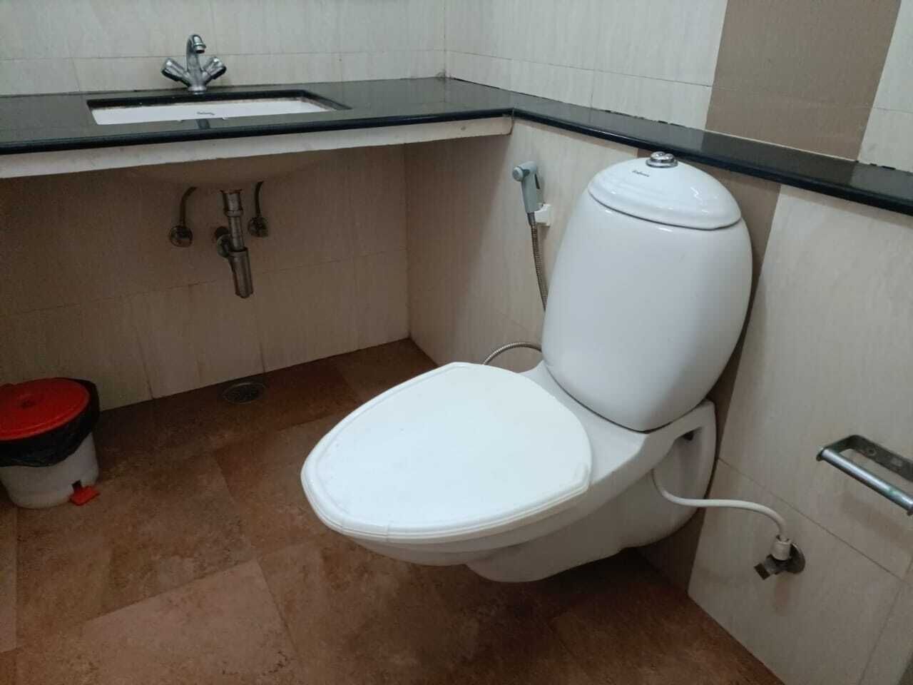 Un baño pequeño con inodoro blanco, lavamanos y un bote de basura rojo.