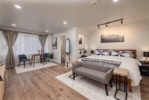 A modern bedroom with a large bed, bedside tables, a sofa, and a small table with chairs. - Downtown Anchorage King Suite + Kitchen (Anchorage)