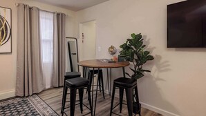 A dining area with a round table, four black stools, a potted plant, and a flat-screen TV mounted on the wall. - Downtown Art Deco - Studio (Anchorage)
