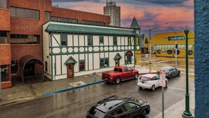 A multi-story building with a green roof and white facade, a red pickup truck parked in front, and a street with cars and a no parking sign. - Downtown Art Deco - Studio (Anchorage)