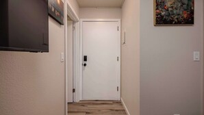 A hallway with a wooden floor, a white door, and a painting on the wall. - Downtown Art Deco - Studio (Anchorage)
