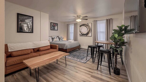 A modern living room with a sofa, a wooden coffee table, a bed, a dining area with a table and chairs, and a ceiling fan. - Downtown Art Deco - Studio (Anchorage)