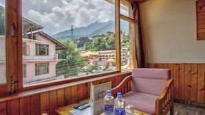 A wooden interior with a table, chairs, and a window offering a view of buildings and mountains. - The Veer Villa (Manali)