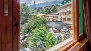 A view from a window overlooking a town with buildings, trees, and a mountain in the background. - The Veer Villa (Manali)