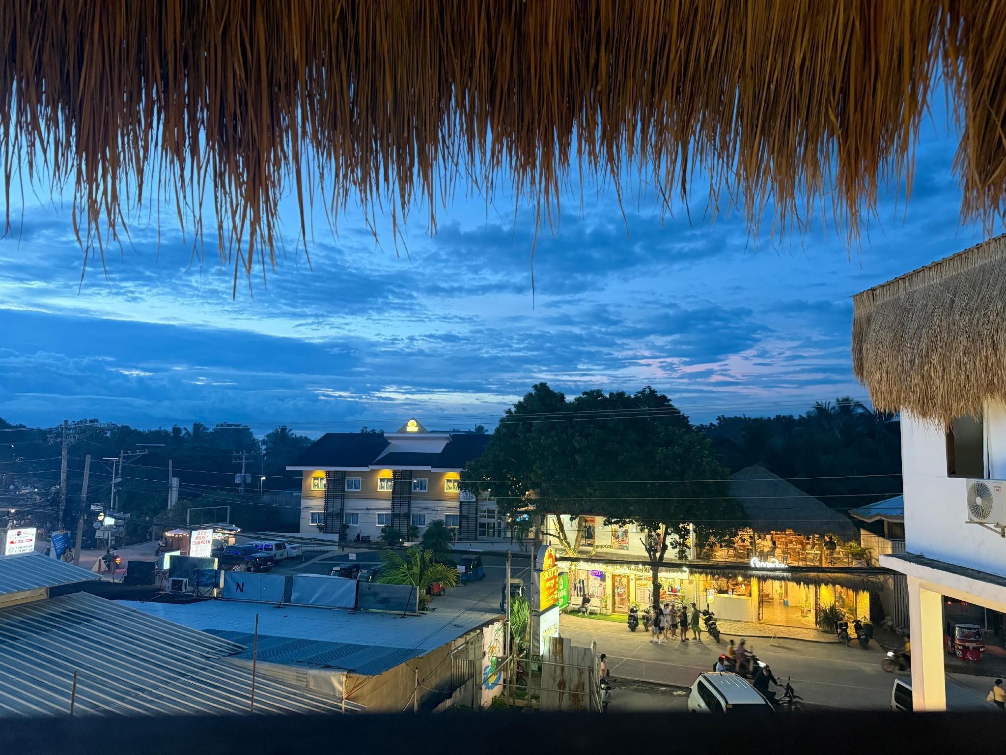 A view of a street with buildings, including a restaurant with outdoor seating and a thatched-roof structure.
