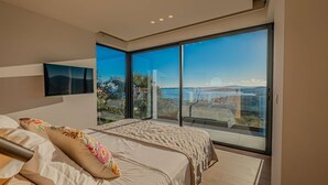 Ein modernes Schlafzimmer mit einem großen Bett, einem an der Wand montierten Fernseher und einem Balkon mit Meerblick.