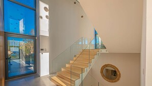 Eine moderne Treppe mit Glastrennwand und Holzwegen, die zu einer Empfangsebene im zweiten Stock mit einem runden Spiegel führt.