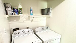Ett tvättrum med två tvättmaskiner från Whirlpool och en hylla ovanför där rengöringsmedel förvaras.
