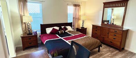 Un dormitorio con cama, escritorio, silla, cómoda y espejo.