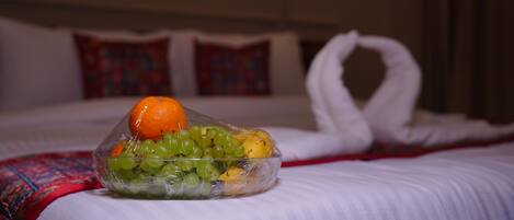 Habitación de hotel con una cama bien hecha, un frutero sobre la cama y una almohada decorativa.
