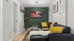 A living room with a black leather sofa, a small round table, a potted plant, and a painting on the wall. - Guest Suite in Edmonton(King bed & Driveway parking),Separate Entrance & Heating (Edmonton)