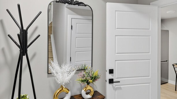 A modern hallway with a white door, a black coat stand, and a wooden console table with decorative items. - Guest Suite in Edmonton(King bed & Driveway parking),Separate Entrance & Heating (Edmonton)