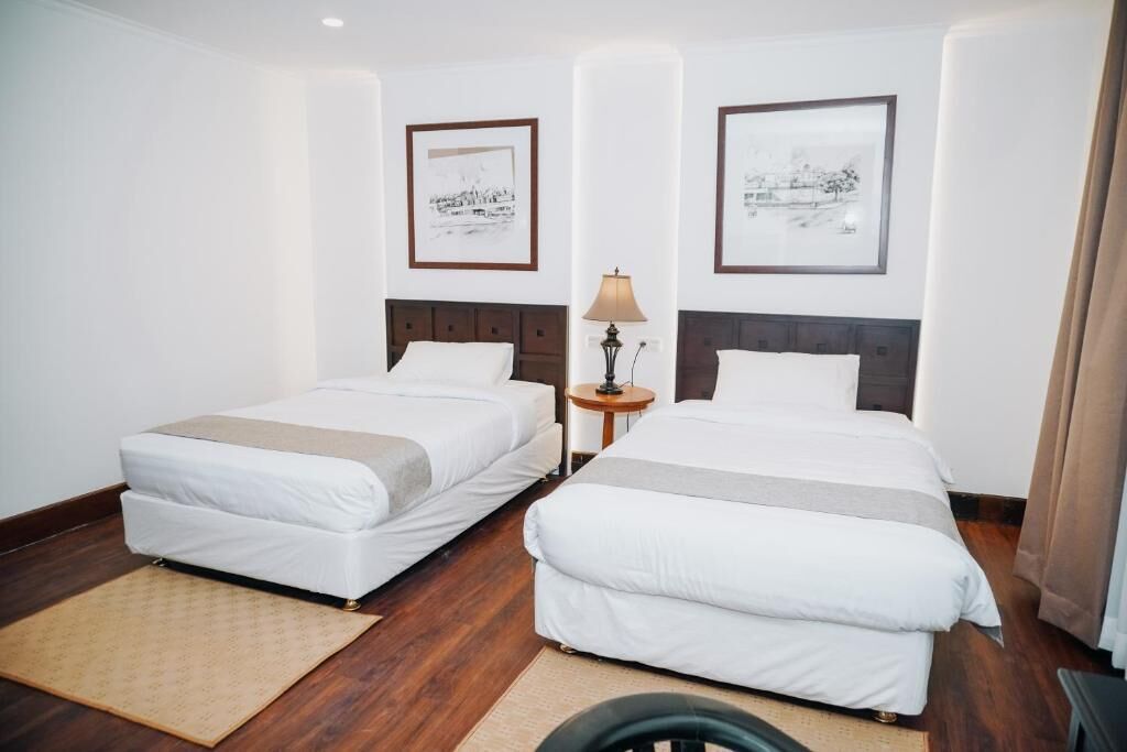 A hotel room with two beds, a small side table with a lamp, and framed artwork on the walls.