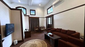 Un salón moderno con un sofá marrón, una mesa de centro, un televisor montado en la pared, una zona de comedor con mesa y sillas, y una alfombra estampada.