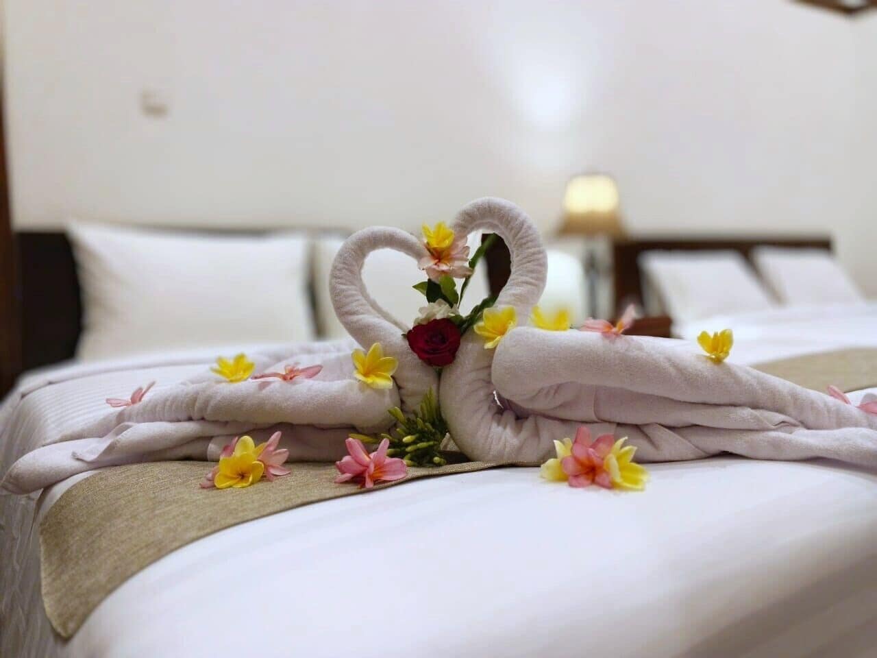 A neatly made bed with a towel swan centerpiece, surrounded by flowers.