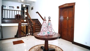 Un vestíbulo amplio con una escalera de madera, una mesa redonda con un adorno y una puerta grande de madera.