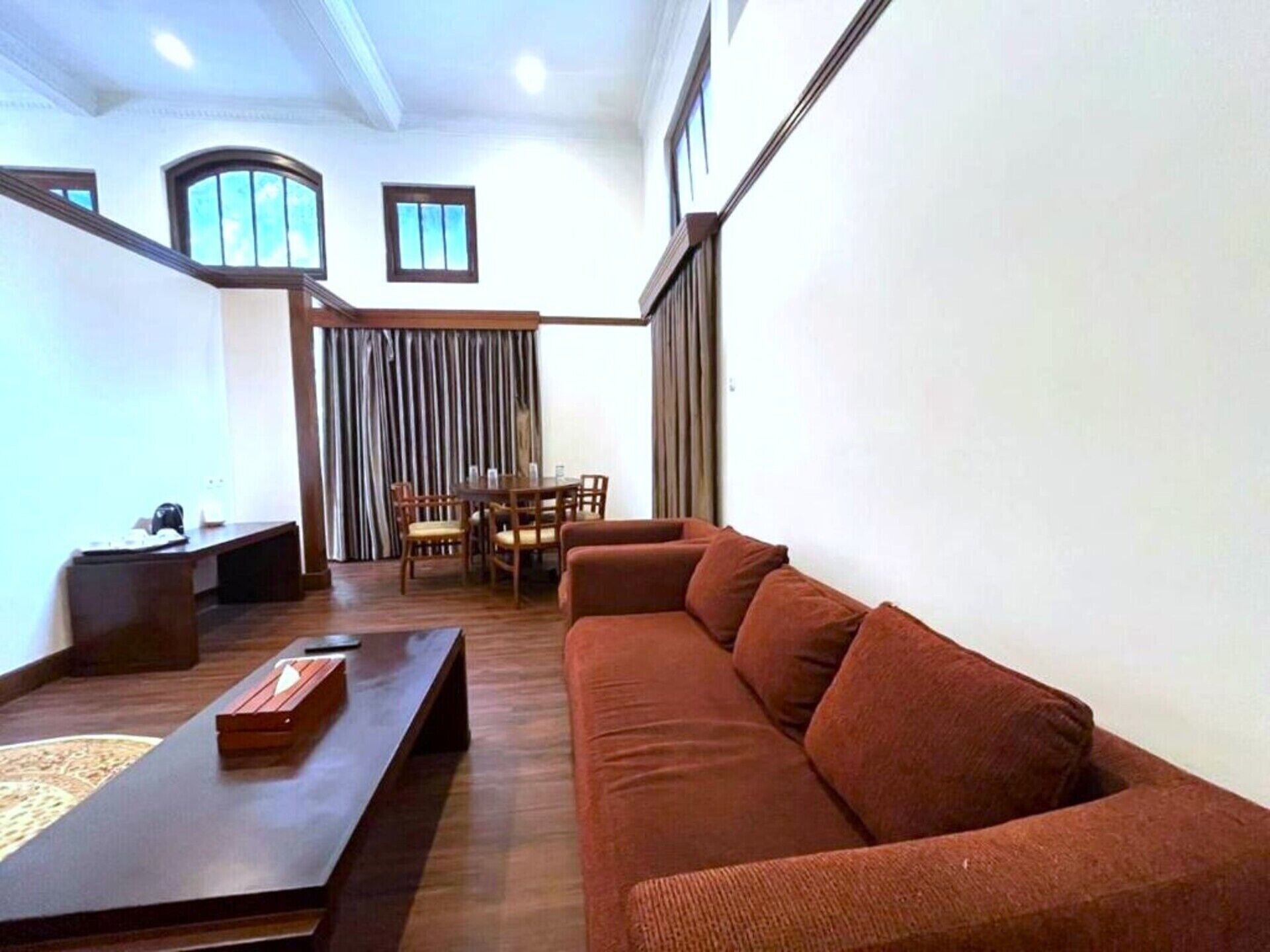 A modern living room with a brown sofa, a wooden coffee table, and a dining area with a table and chairs.