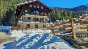Ein mehrstöckiges Holzhaus mit Balkonen, umgeben von Schnee und bewaldeten Bergen.