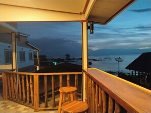 A wooden balcony with a view of the sea and a distant shoreline.