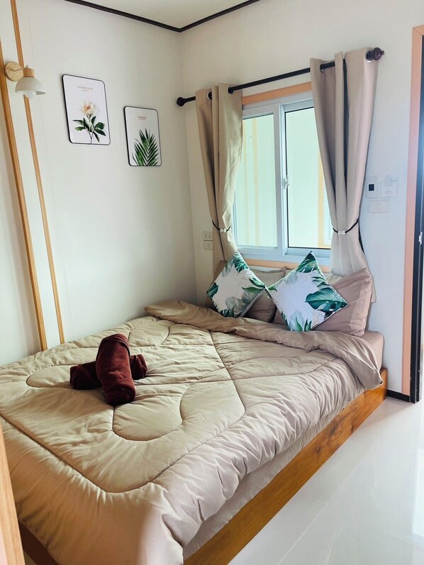 A single bed with a beige quilt, a wooden headboard, and a window with curtains. There are two wall-mounted light fixtures and two framed botanical prints. - RabeangPhan Homestay Libong (Ko Libong)