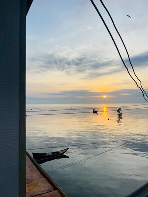 A sunset view from a window overlooking a calm sea with a boat and a bird in the sky. - RabeangPhan Homestay Libong (Ko Libong)