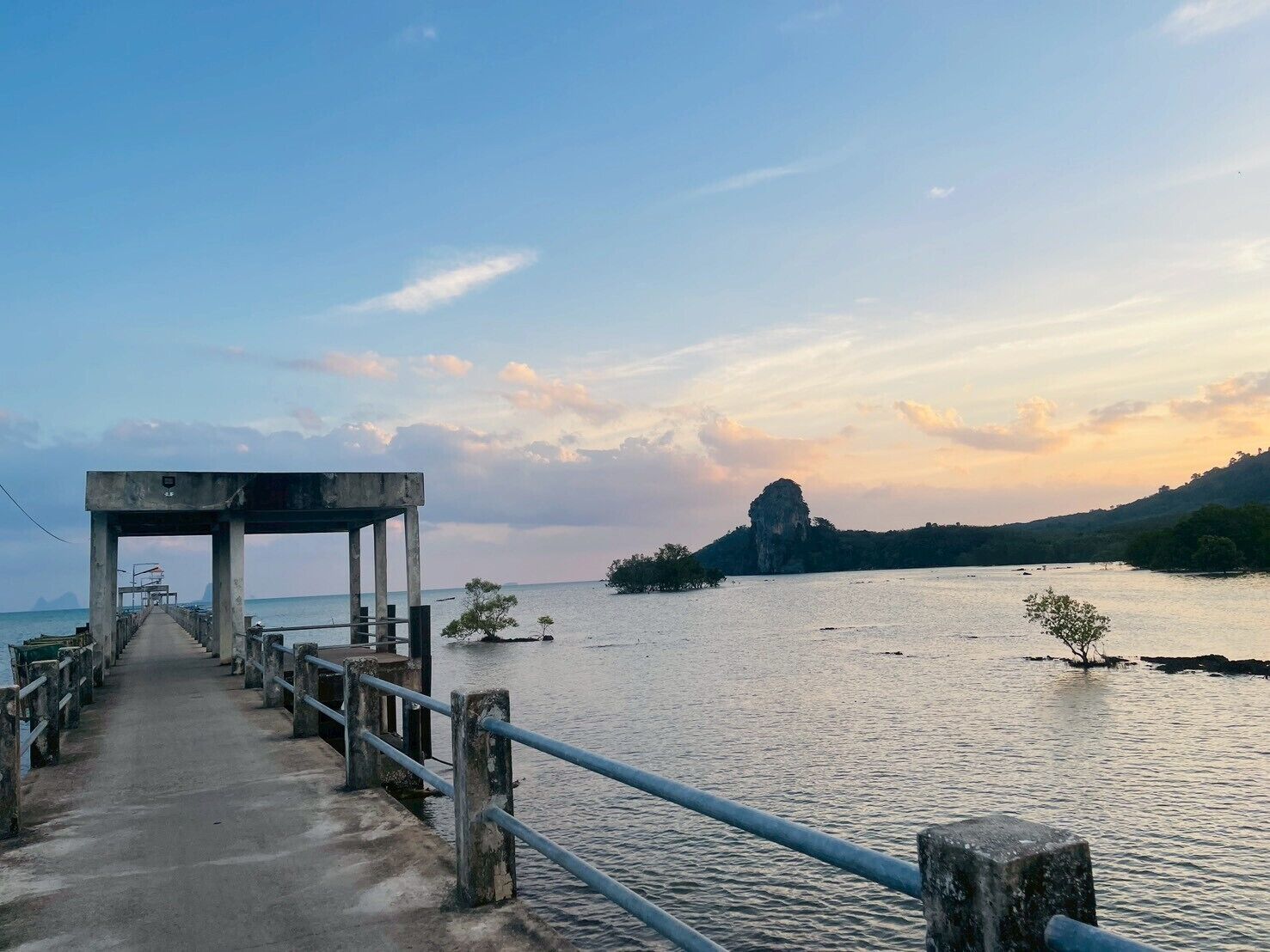 Un muelle que conduce a una masa de agua con una isla rocosa en la distancia y un cielo despejado.