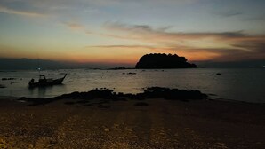 A beach with a boat and a small island in the distance during sunset.