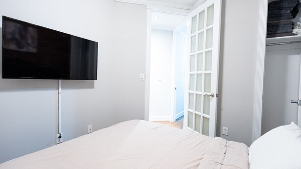 A bedroom with a bed, a television mounted on the wall, and a closet with a folded towel. - Hells Kitchen 2 Bedroom Retreat (New York)