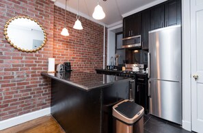 A kitchen with a brick wall, stainless steel appliances, and pendant lighting. - Hells Kitchen 2 Bedroom Retreat (New York)