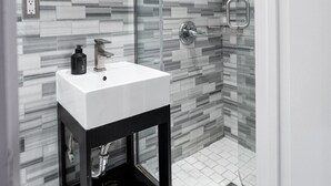 Un baño moderno con cabina de ducha de vidrio, lavamanos blanco y suelo de baldosas.