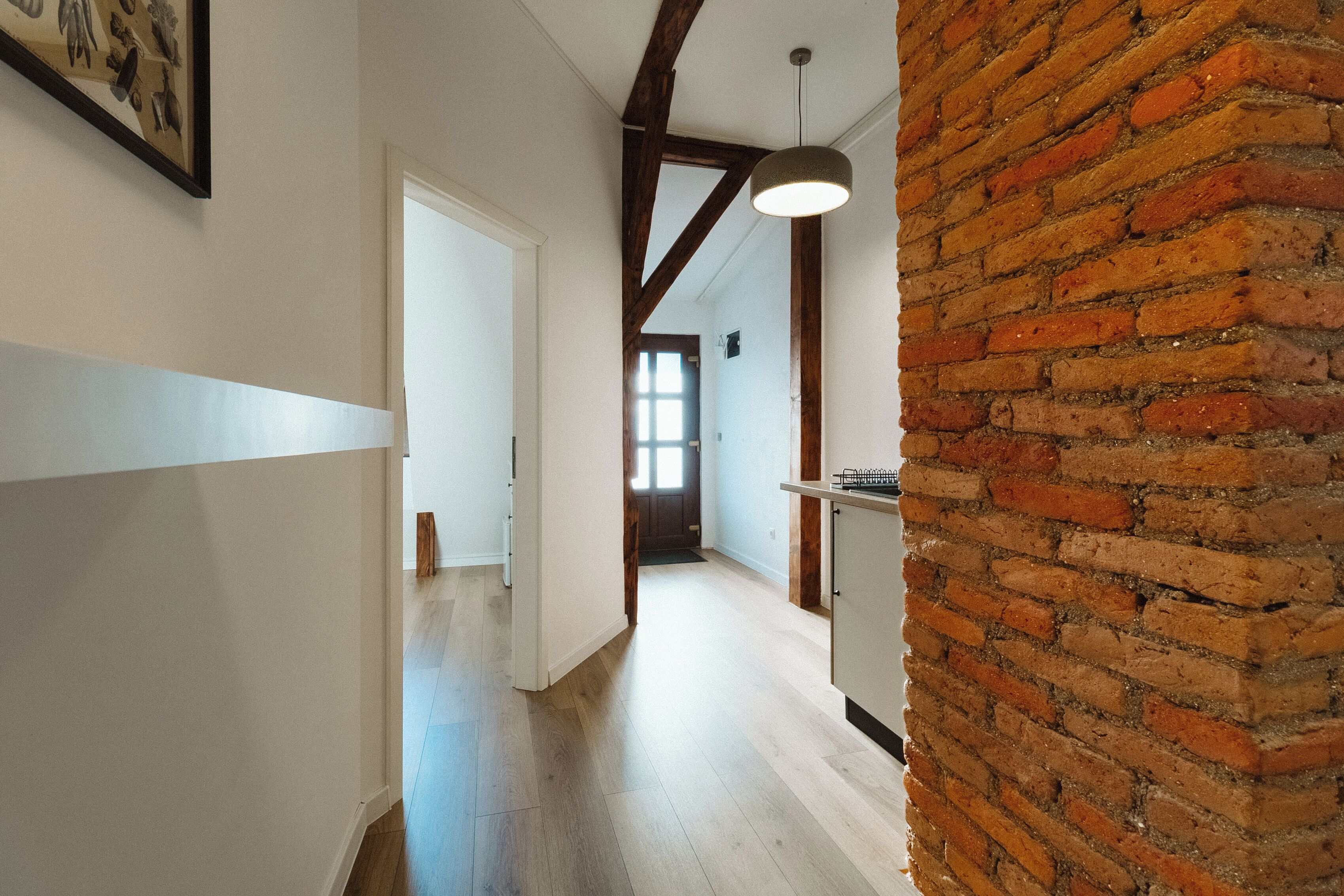 A hallway with a wooden floor, white walls, and exposed brick on one side.