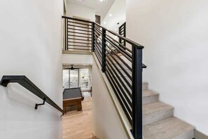 A staircase with black railings, a wooden bench, and a view of a room with a large window.