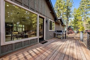 A wooden deck with a grill, large windows, and a dining area visible through the glass.