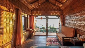 A room with a thatched roof, wooden walls, a sofa, a table, and a view of the sea. - Sampan Beach Resort Saintmartin (Saint Martin's Island)