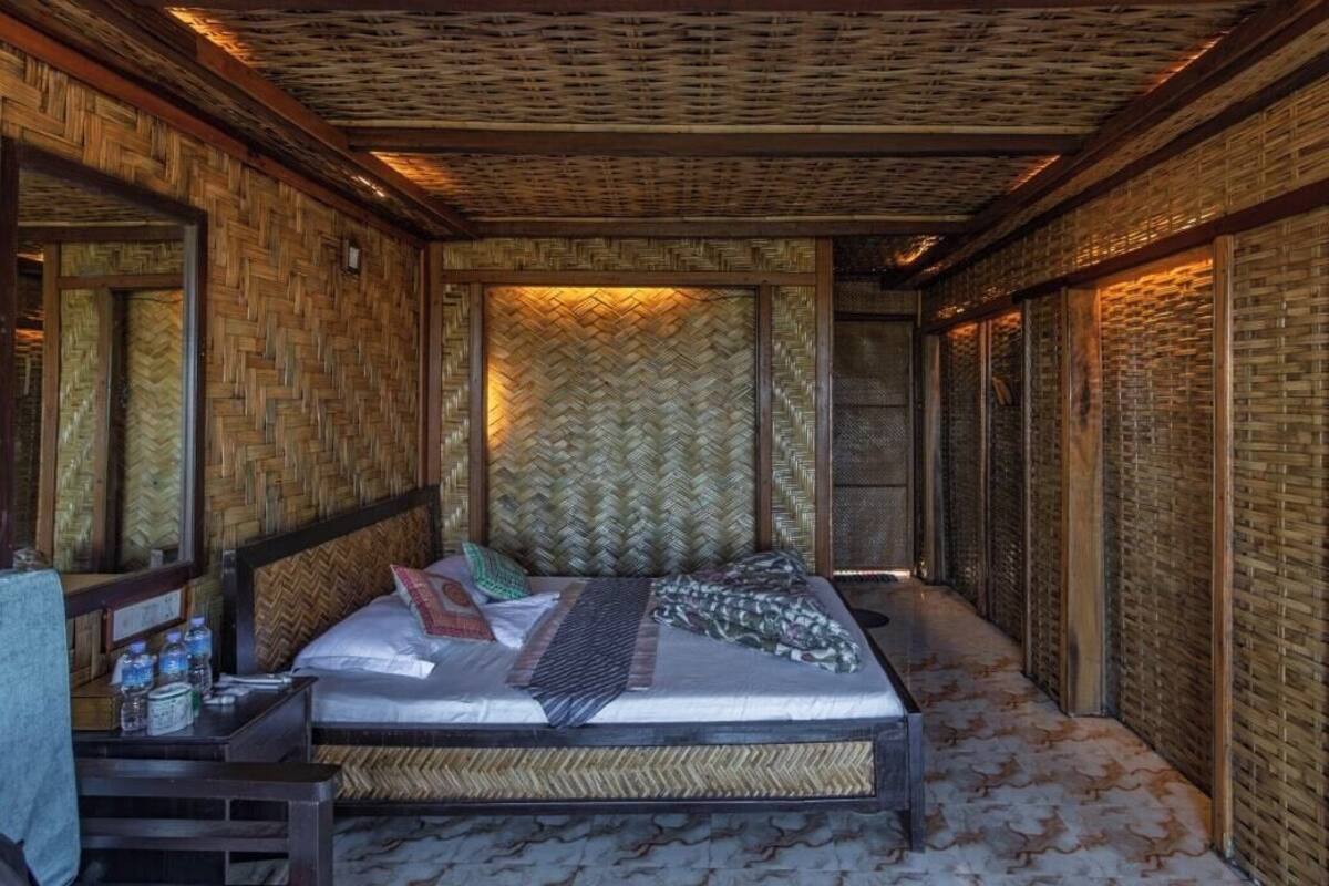 A room with a bed, a nightstand, and a large mirror. The walls are covered with woven mats, and there is a woven ceiling.