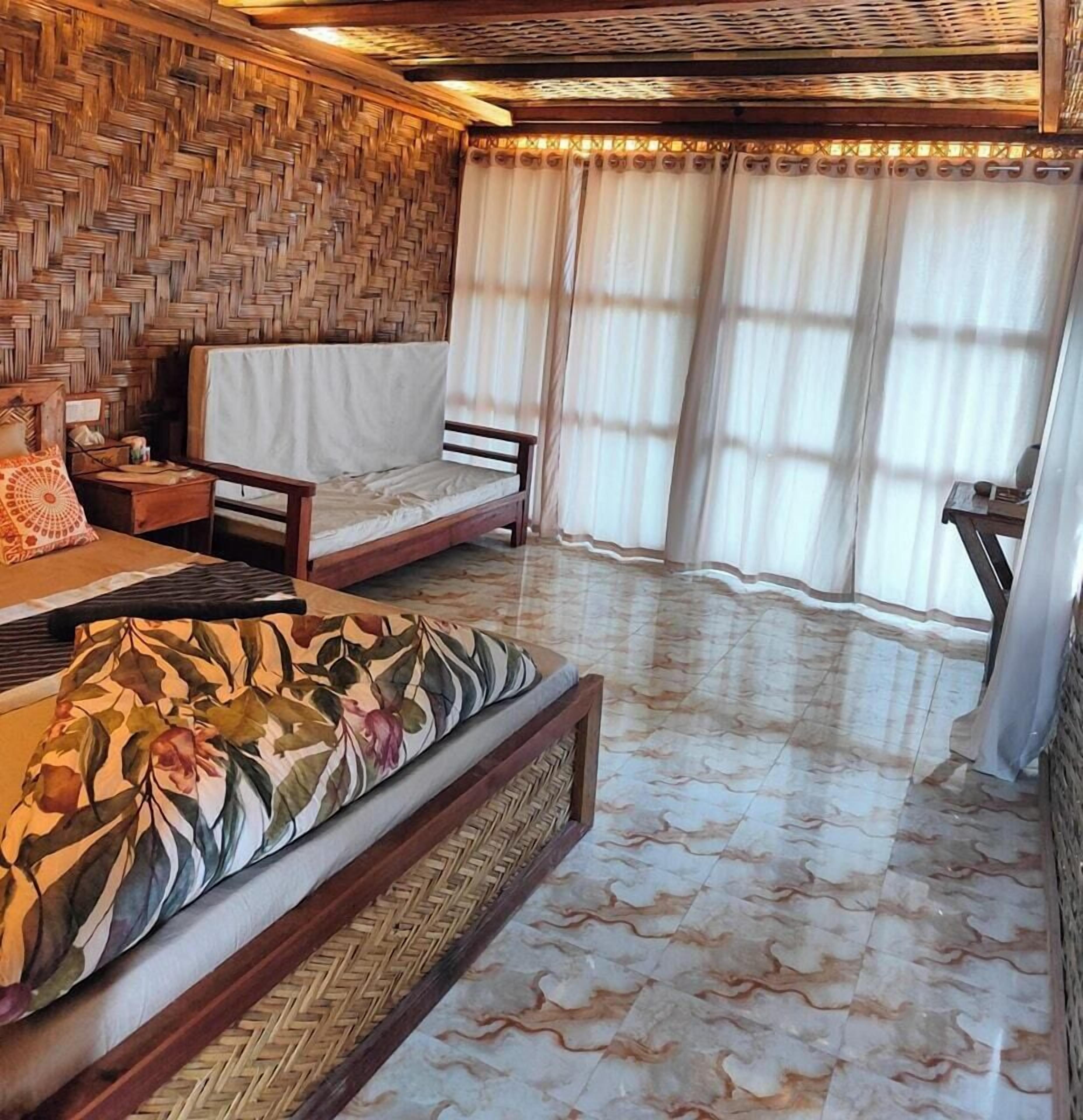 Habitación con pared tejida, un sofá, una cama y vistas al exterior a través de amplios ventanales.