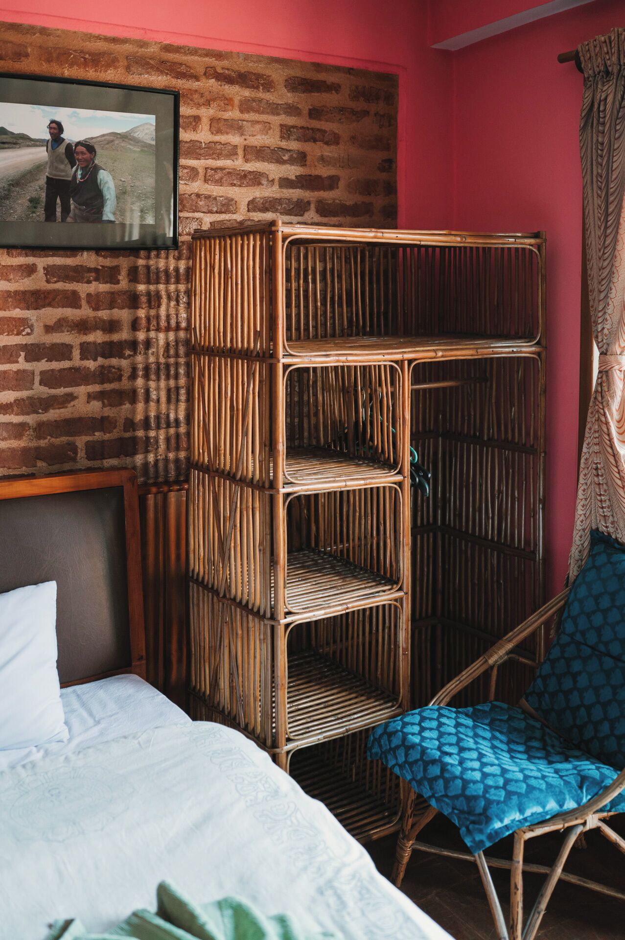 Una habitación con cama, una silla de mimbre y un estante en la pared.