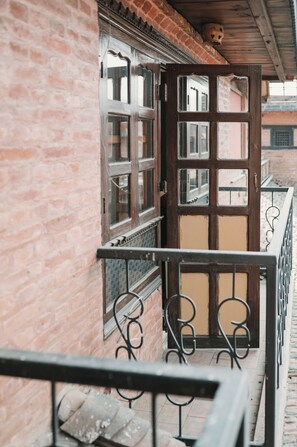 A wooden door with glass panels, a balcony with metal railings, and a brick wall. - New Shiva Guest House (Bhaktapur)