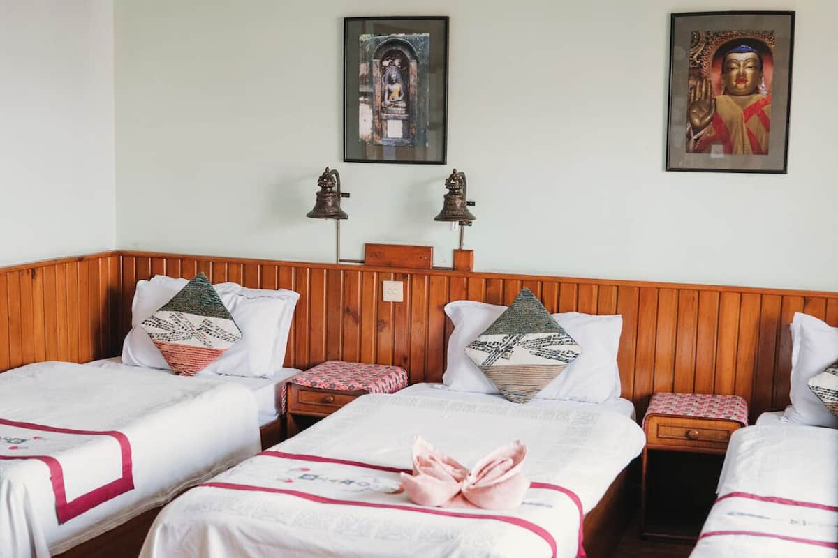 Een hotelkamer met drie houten bedden, wit beddengoed en twee aan de muur bevestigde religieuze beelden.