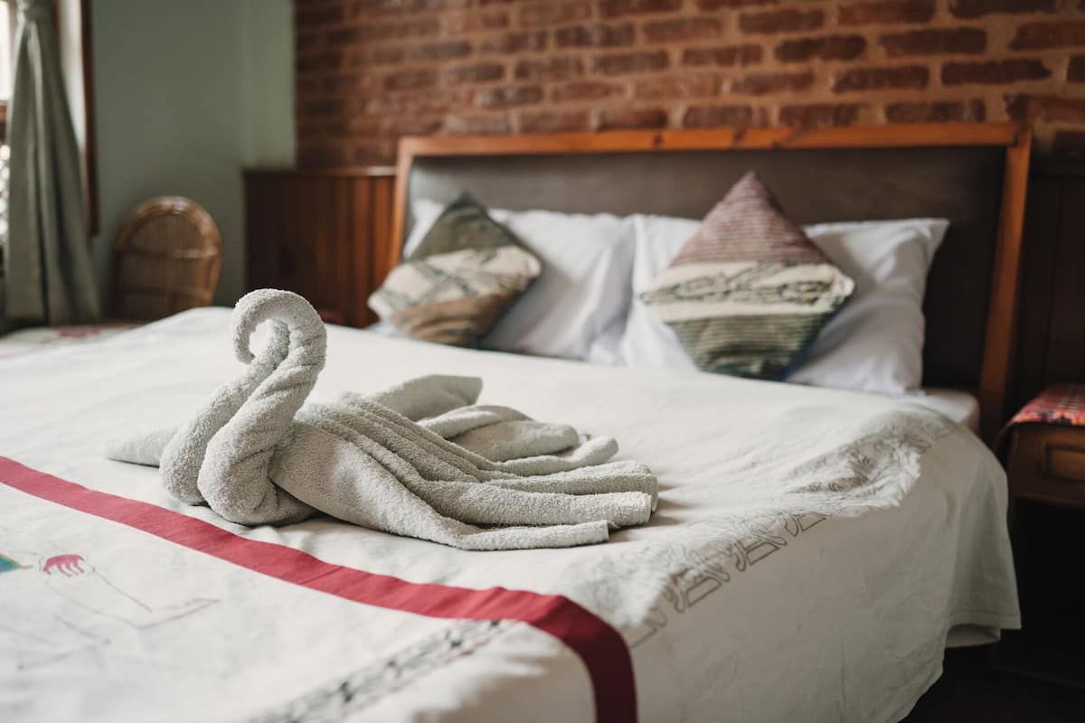 Een net opgemaakt bed met een zwaanvormige handdoek, een bakstenen muur en een houten hoofdeinde.