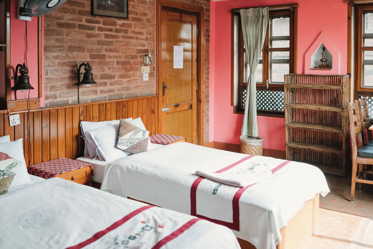 Een kamer met twee bedden, een houten garderobe, een bakstenen muur en een raam met gordijn.