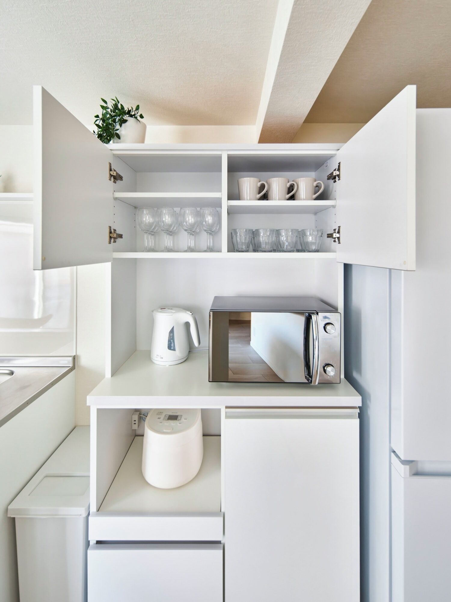 A compact kitchen with white cabinetry, a microwave, a kettle, and glassware.