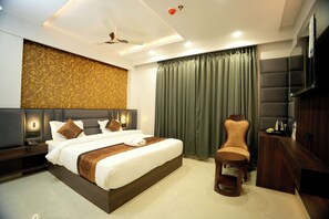 A modern hotel room with a large bed, a vanity with a mirror, a chair, and a television. - Hotel Shri Vinayak (Varanasi)