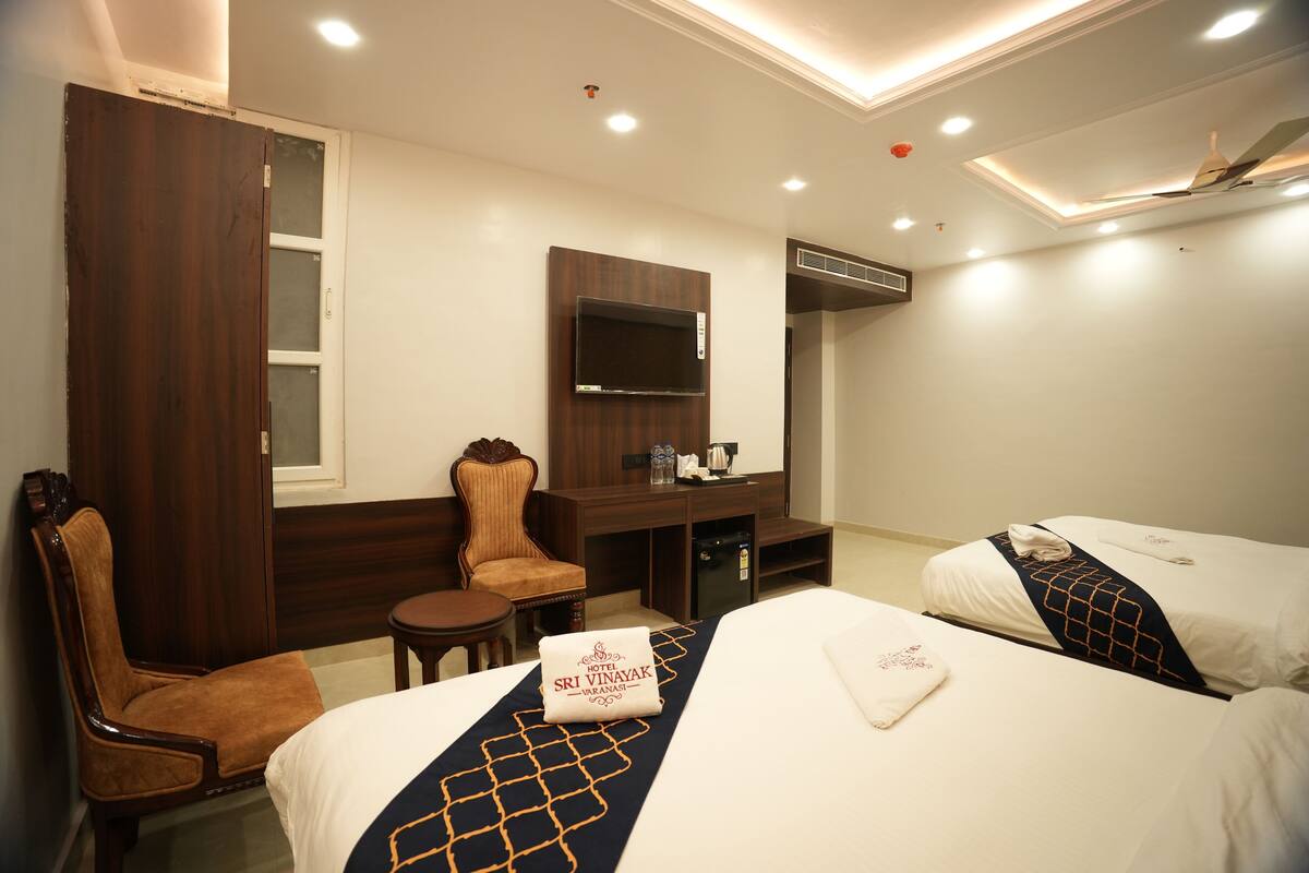 A hotel room with two beds, a desk, a chair, and a TV.