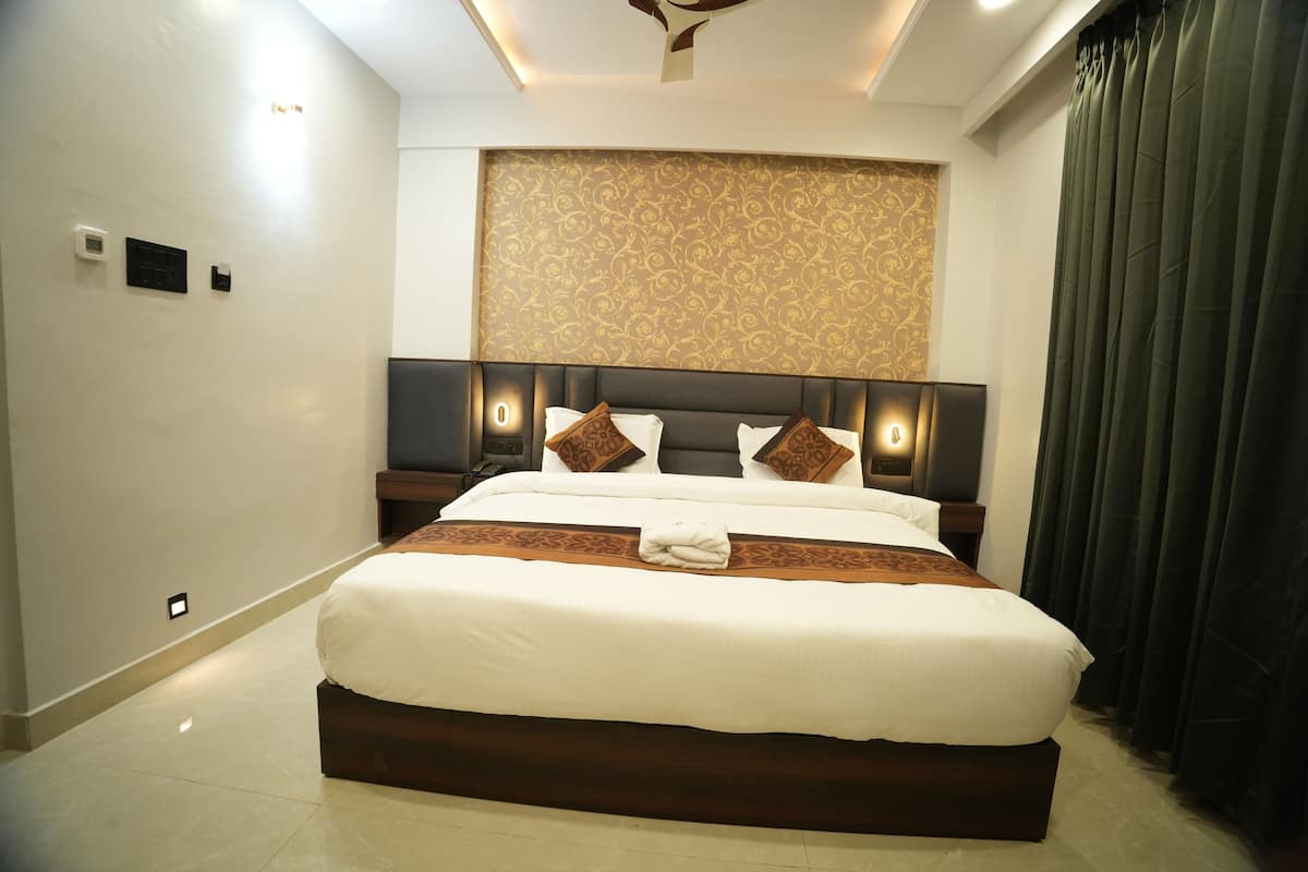 A modern hotel room with a large bed, a headboard with integrated lighting, a decorative wall panel, and a dark curtain.
