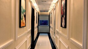 A hallway with framed artwork on the walls, a polished floor, and a ceiling with recessed lighting. - Hotel Shri Vinayak (Varanasi)