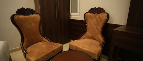 Two upholstered chairs with wooden frames and a round table in a room with a wooden wardrobe and a window.