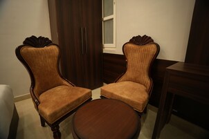 Dos sillones tapizados con armazones de madera y una mesa redonda en una habitación con un ropero de madera y un ventanal.