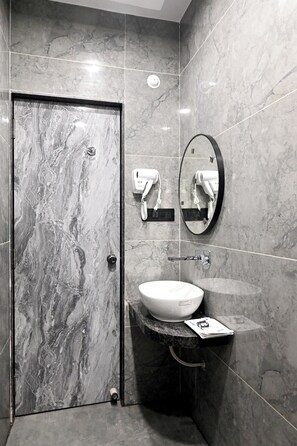 A modern bathroom with a marble floor and walls, a white sink, a round mirror, and a towel rack. - Hotel Shri Vinayak (Varanasi)